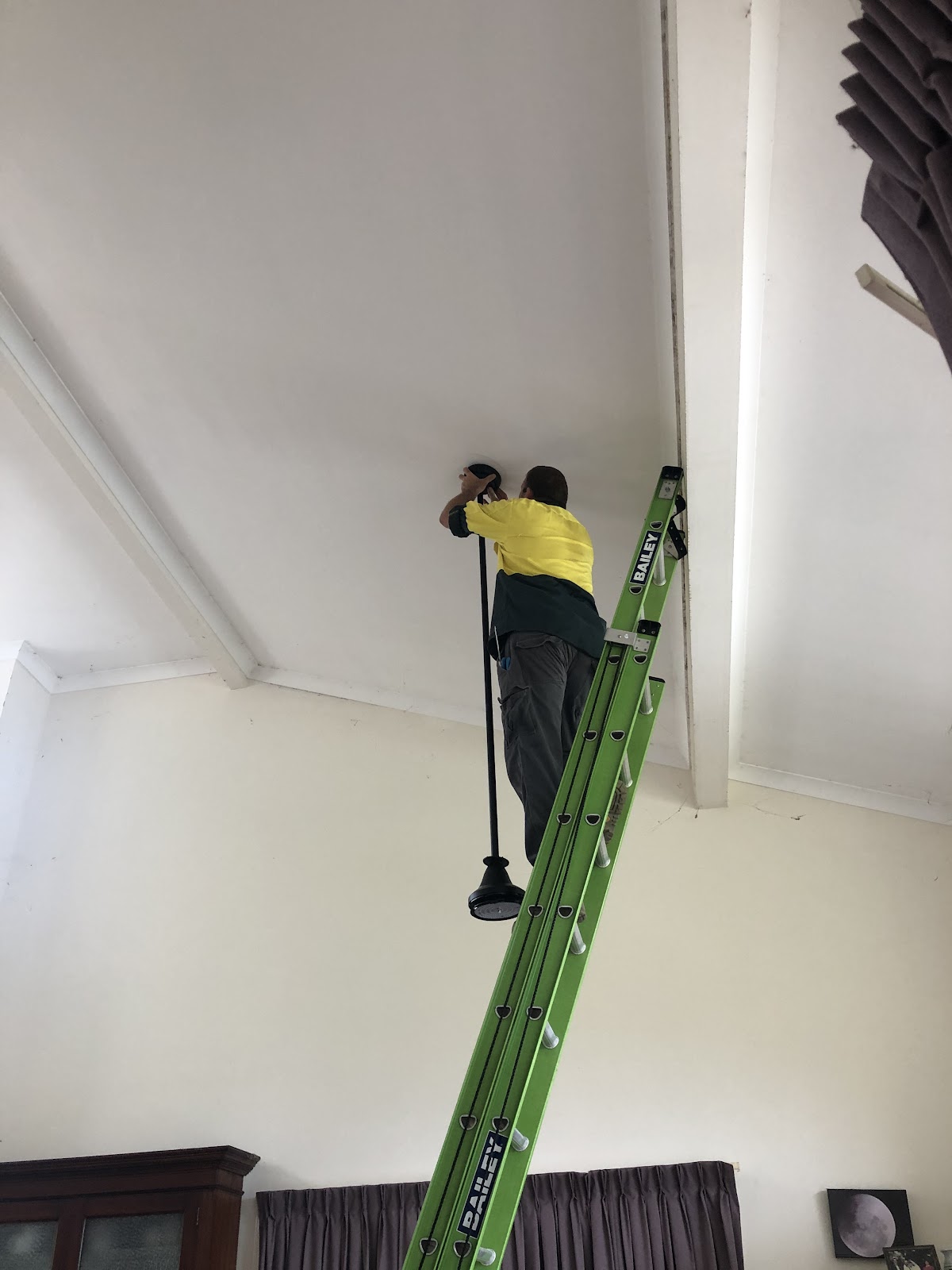 Charlie up a ladder fitting a light to a high ceiling