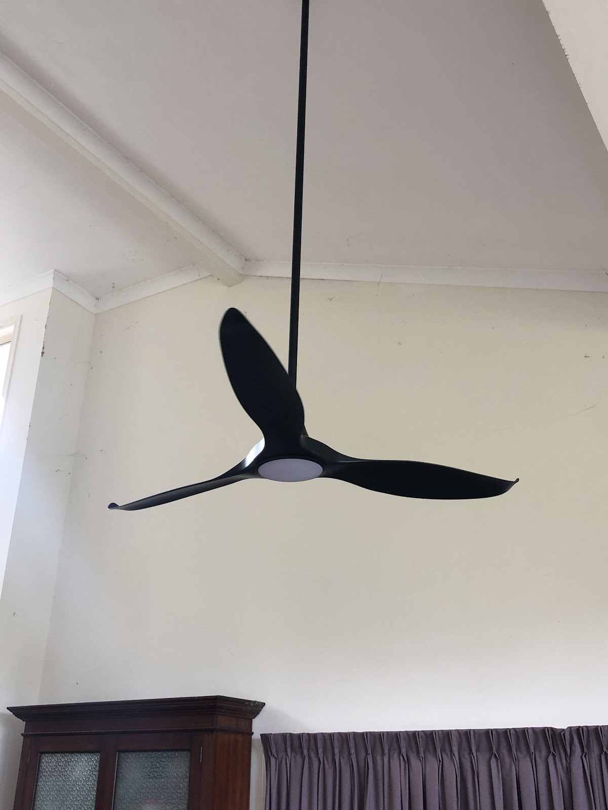 Black three blade ceiling fan with a light on a long downrod under a raked ceiling